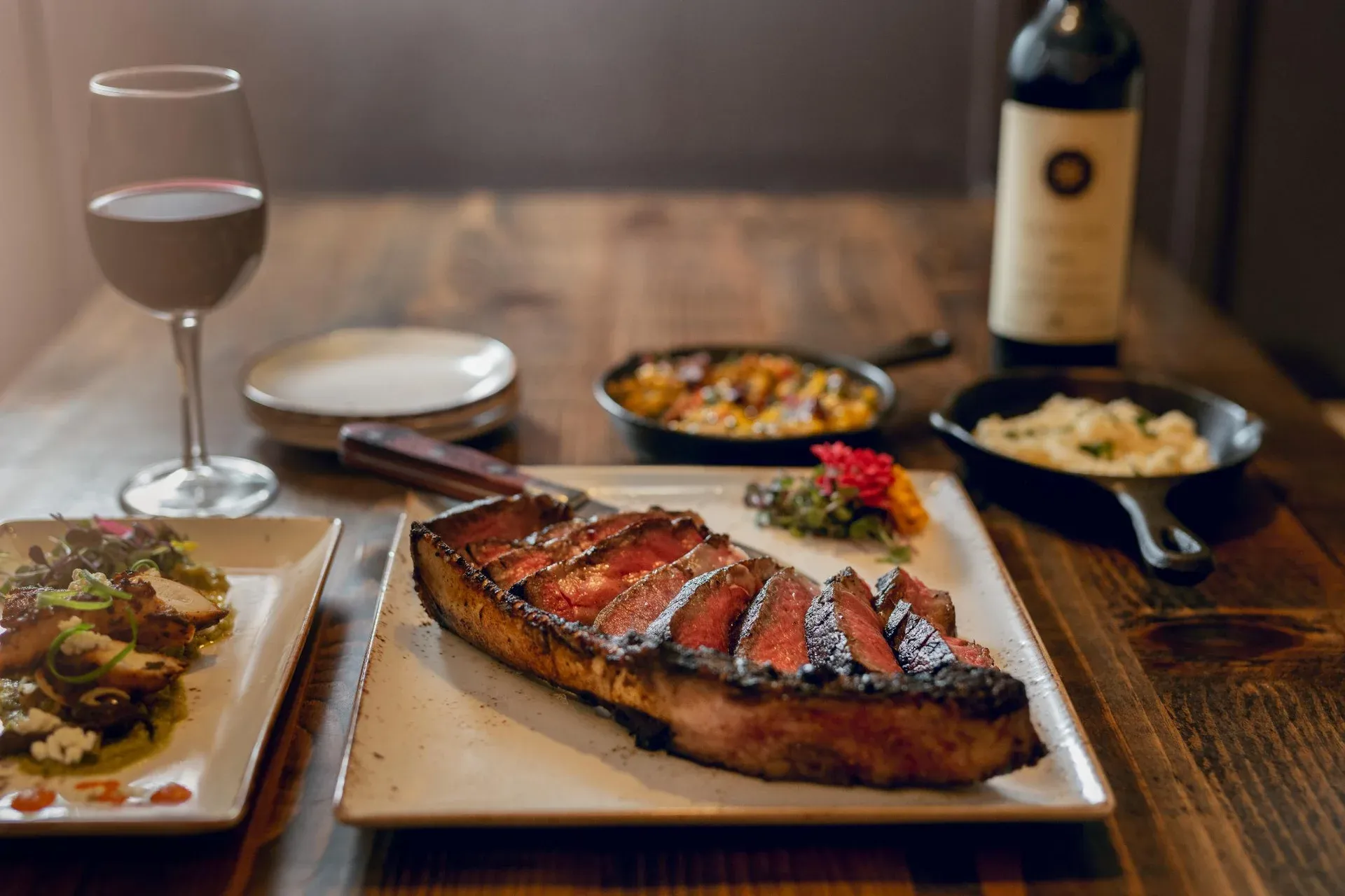 A sliced bone-in steak on a plate with a glass and bottle of red wine